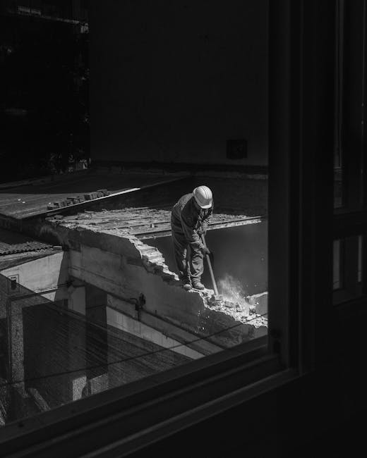Two individuals are walking through a covered corridor of a modern building, with one of them wearing a high-visibility red and black jacket featuring the logo of a waste management company, while the